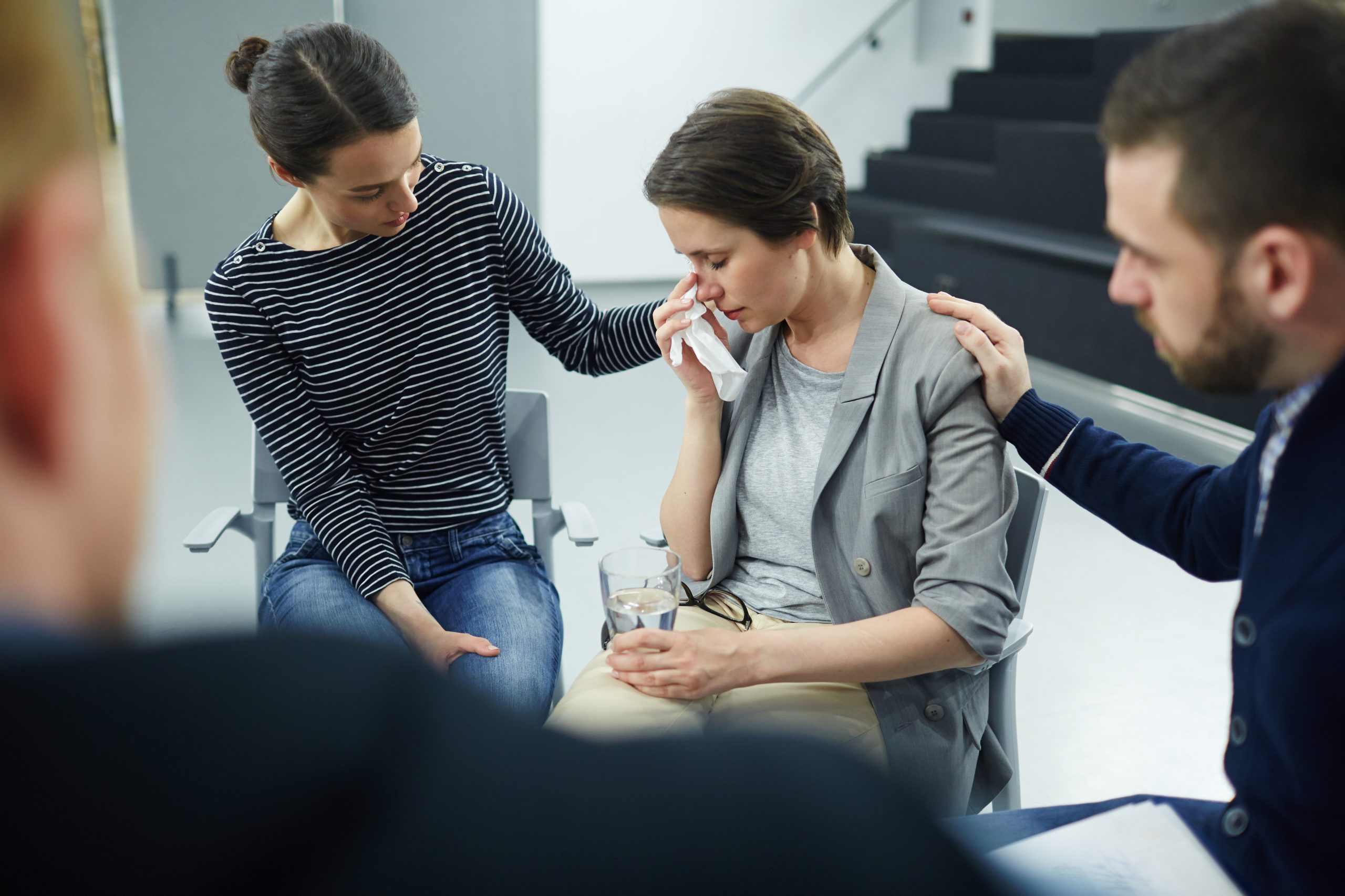 Stressed woman wiping her tears with a tissue while friends comfort her with support.